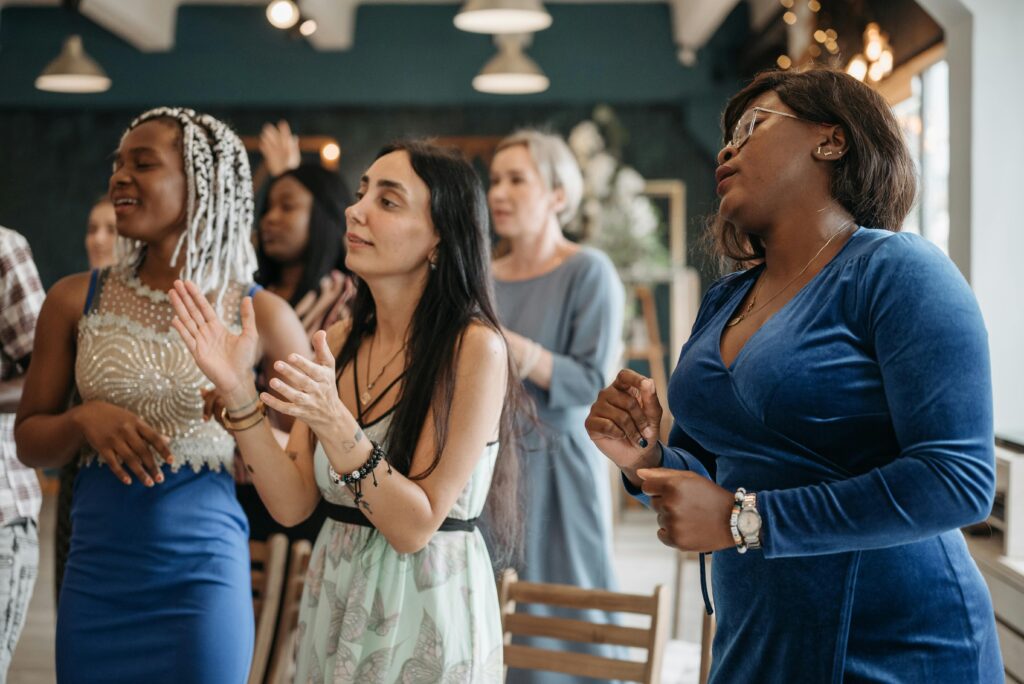 A group of diverse women singing indoors, expressing joy and unity.